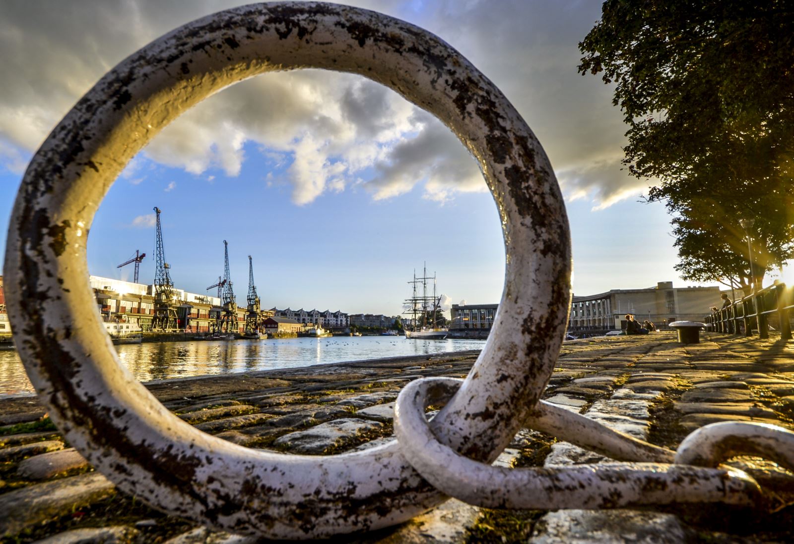 A dockyard scene featuring an ancient small ship and photographed using the circular metal mooring ring as a frame